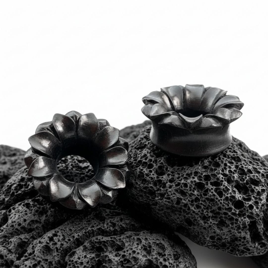 Pair of dark Areng wood tunnels with a detailed carved lotus design, shown as organic gauges for stretched lobes.