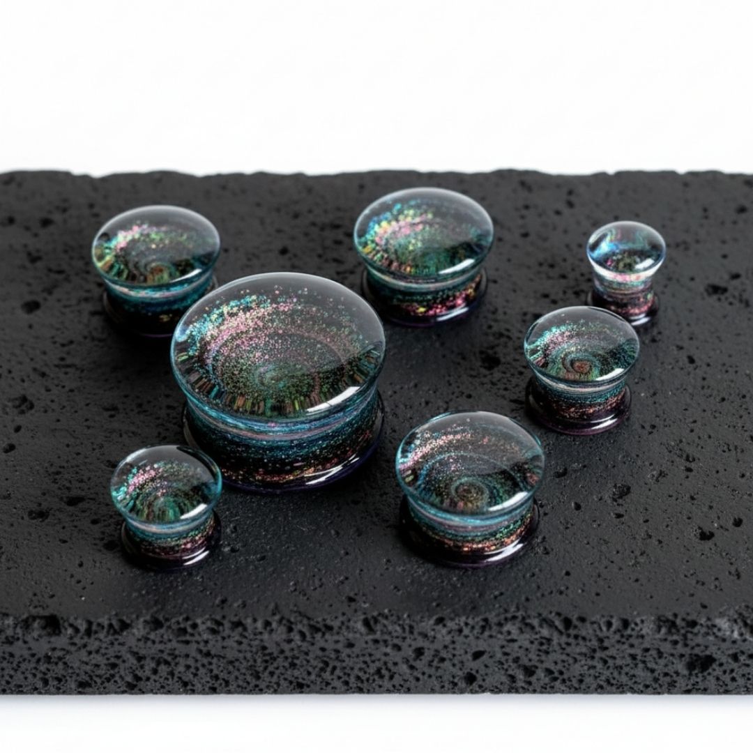 A pair of Glass Cosmos Plugs (6mm-25mm) on stone against a clean white background.