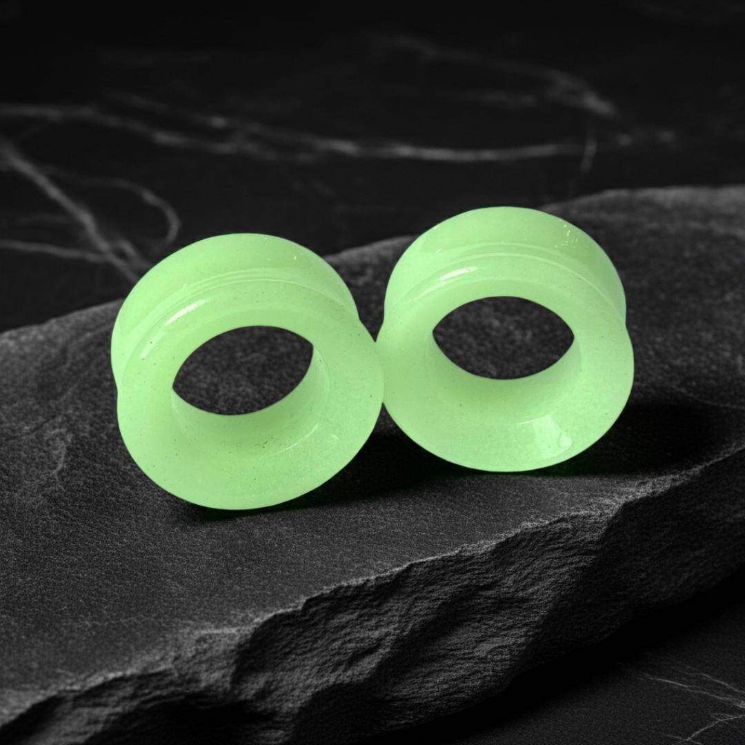 Glow in the dark moonstone tunnels for stretched ears on a gritty black stone background