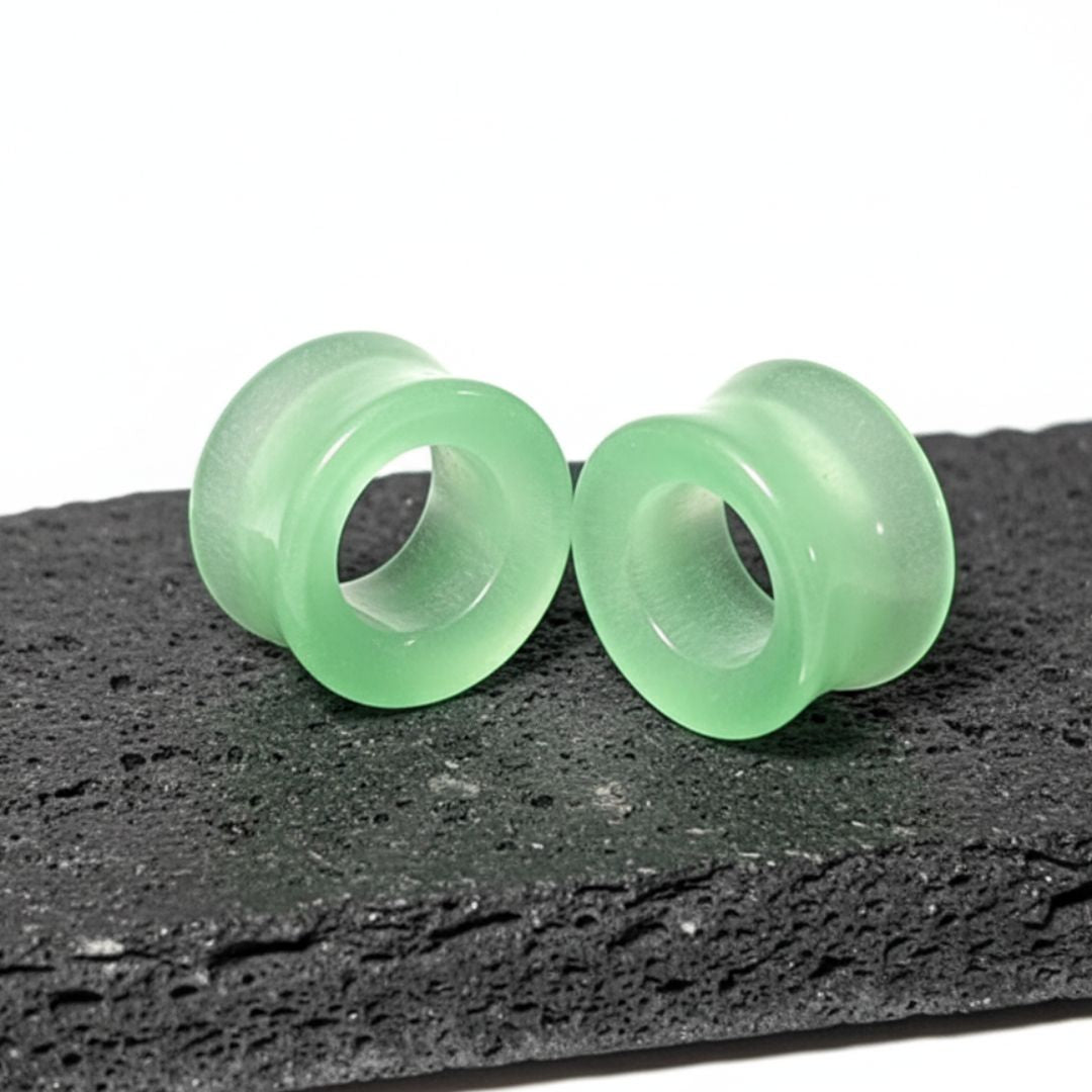 Close-up shot of a pair of polished Green Dragon Eye Stone Tunnels, showing the swirling green on a black volcanic stone