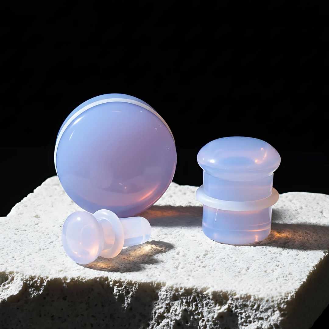 Set of pink purple glass earplugs on a textured surface with a dark background