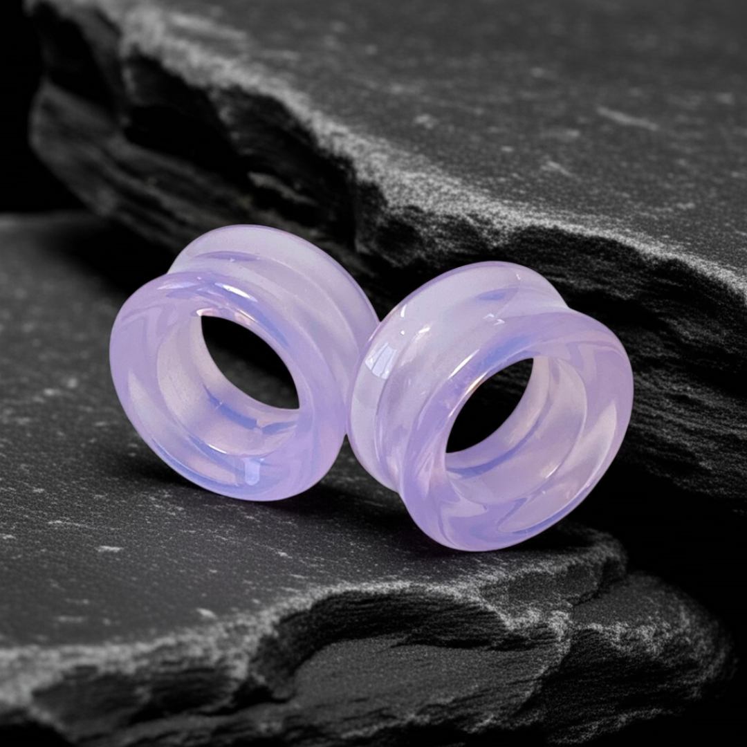 Pair of light purple ear gauges on a dark stone surface