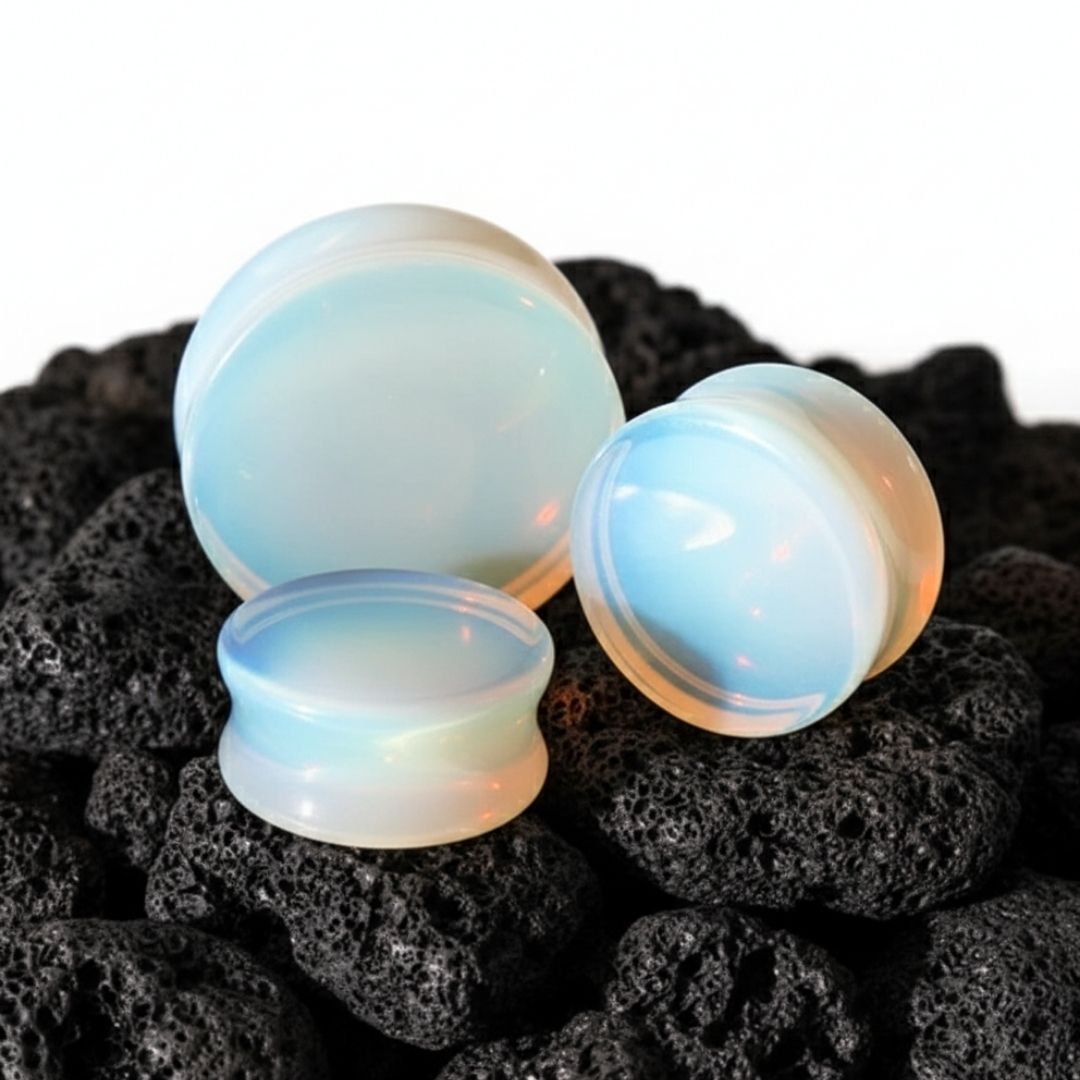 Double-flared opalite glass plugs for stretched ears. Milky white gauges glowing blue, displayed on a dark surface.