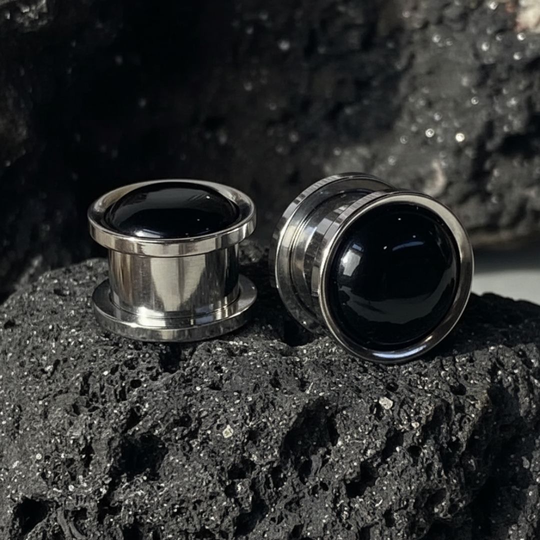 Two metallic earplugs with black centers on a dark textured surface