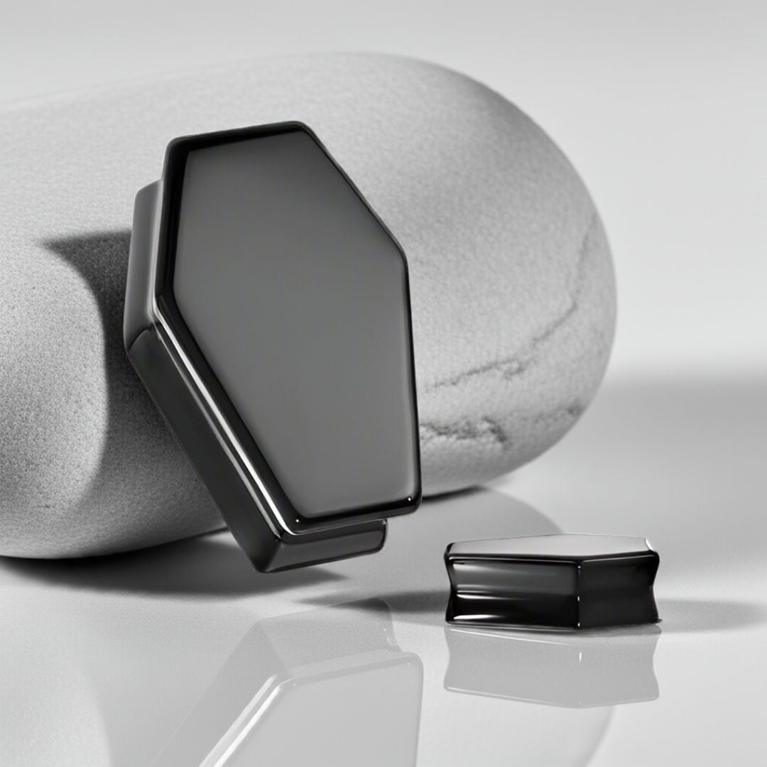 air of obsidian coffin-shaped ear plugs with sleek black finish and sharp, angular design on a stone surface