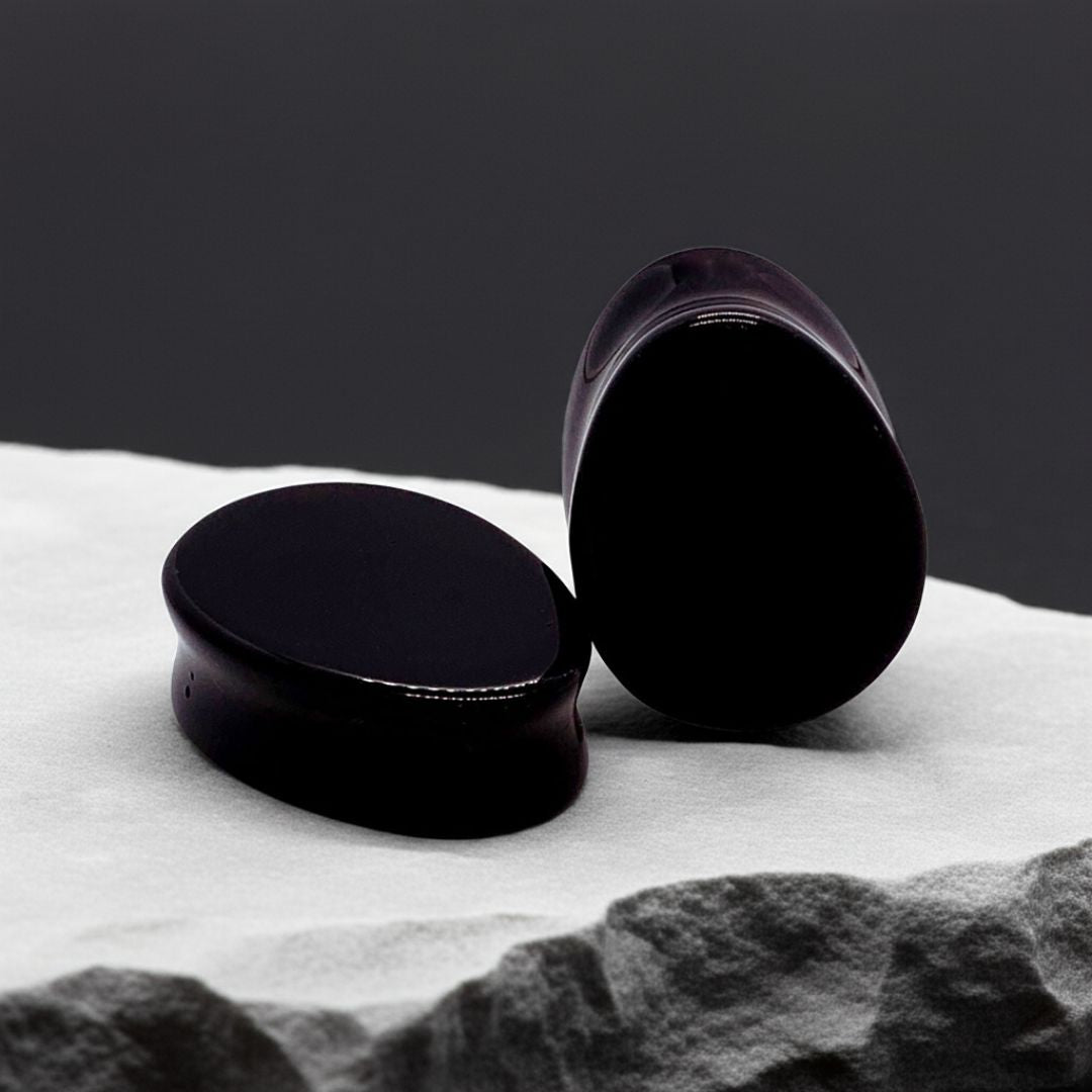 Pair of obsidian teardrop-shaped ear plugs with glossy black finish and smooth curves, shown on a dark stone backgroun