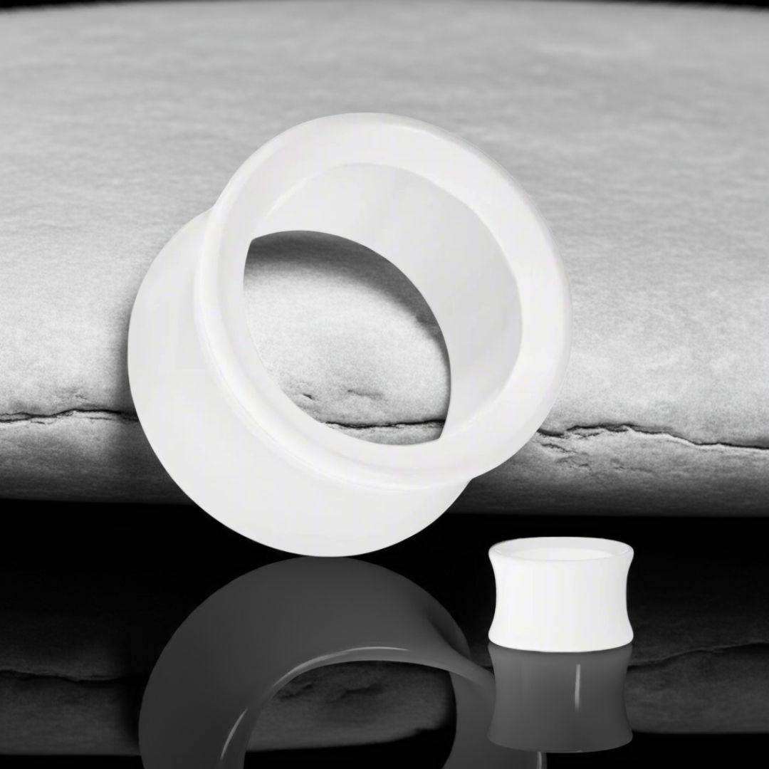 Pair of white acrylic ear tunnels with smooth, glossy finish and lightweight design, displayed on a dark stone surface