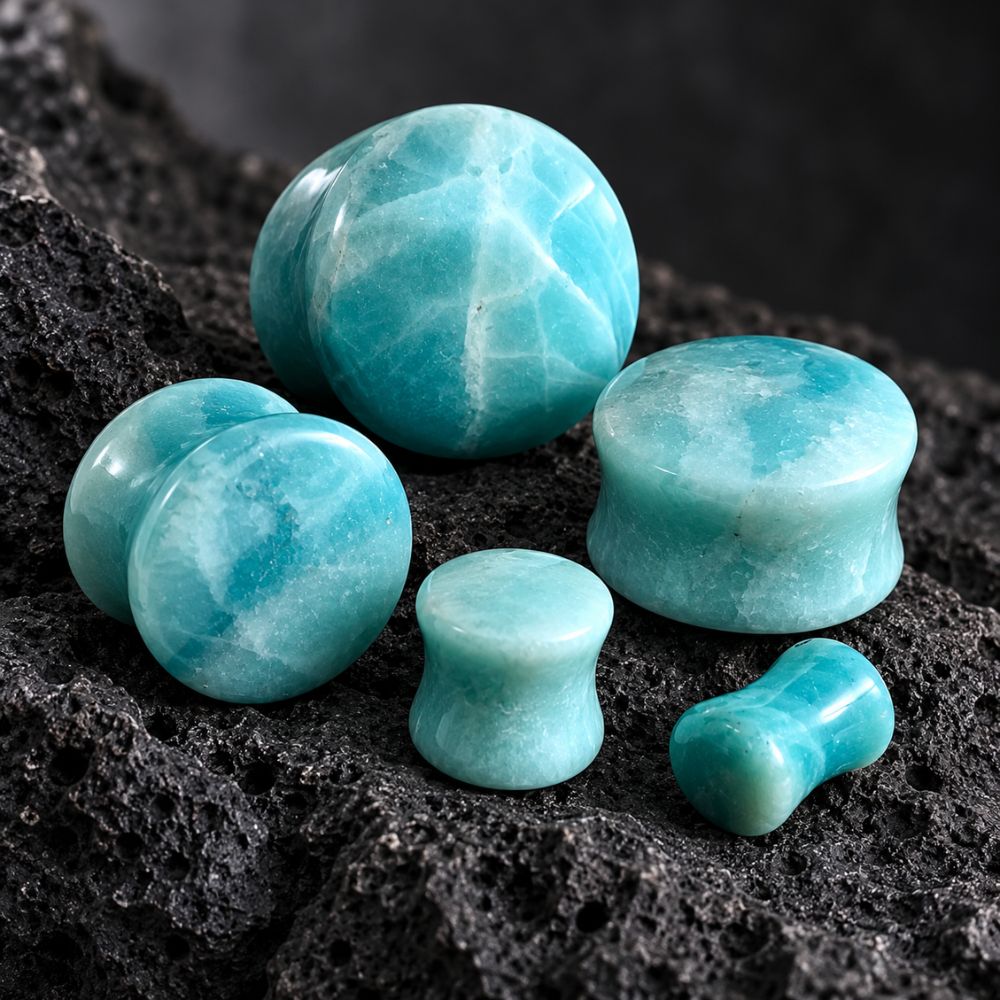 A set of turquoise-blue polished stone plugs and domes arranged on a dark porous rock surface. The pieces include round, cylindrical, and dumbbell-shaped forms with a marbled aqua coloration.