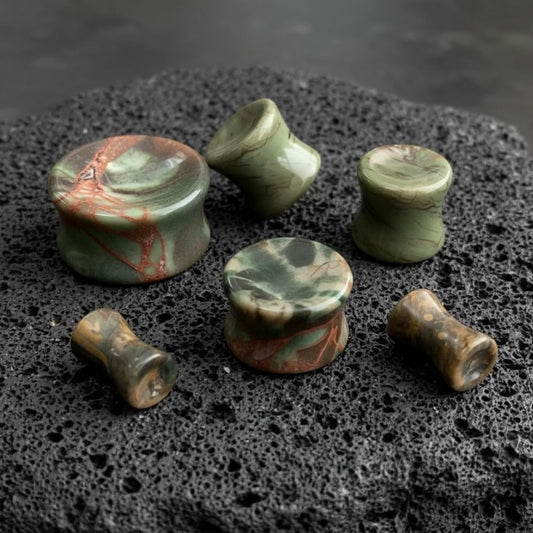 A pair of Amber Agate Stone plugs (6mm-25mm) on dark volcanic rock with sharp side lighting.