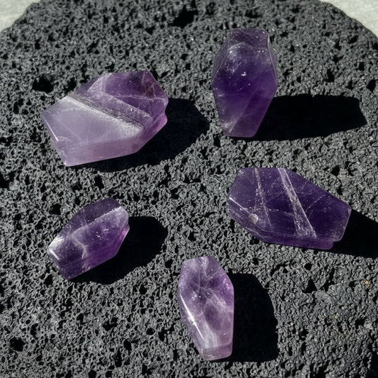 Amethyst Stone Coffin Plugs (6mm-25mm) on dark volcanic rock with sharp side lighting.