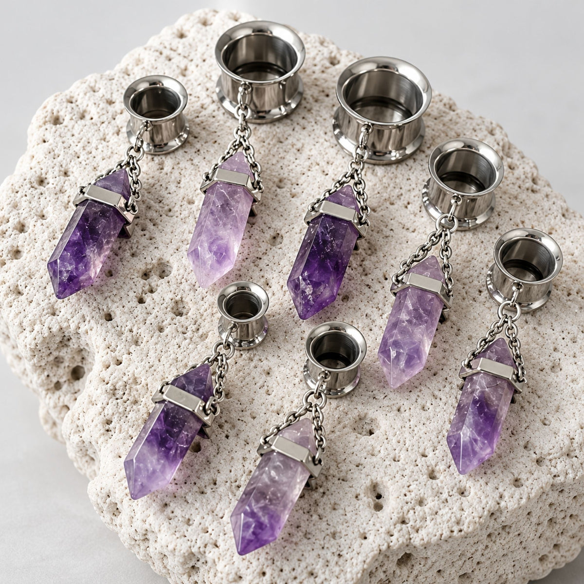A pair of Steel Amethyst Dangle Tunnels on rock against a clean white background.