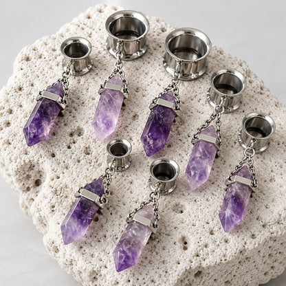 A pair of Steel Amethyst Dangle Tunnels on rock against a clean white background.