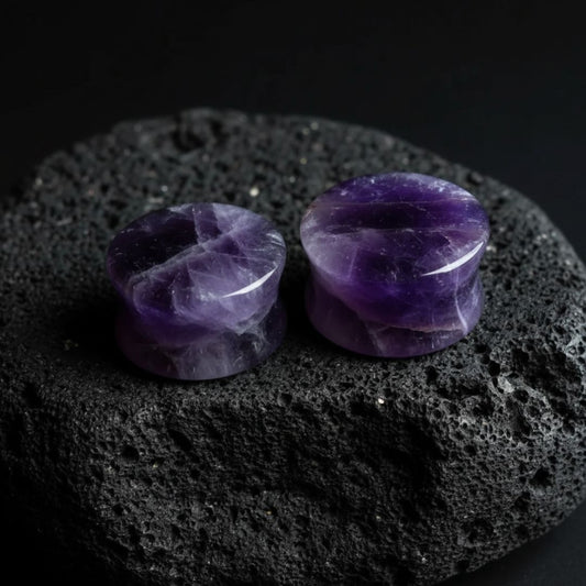 Pair of deep purple Amethyst stone plugs, double flare style, shown against a dark, textured background. Stretched ear jewelry.