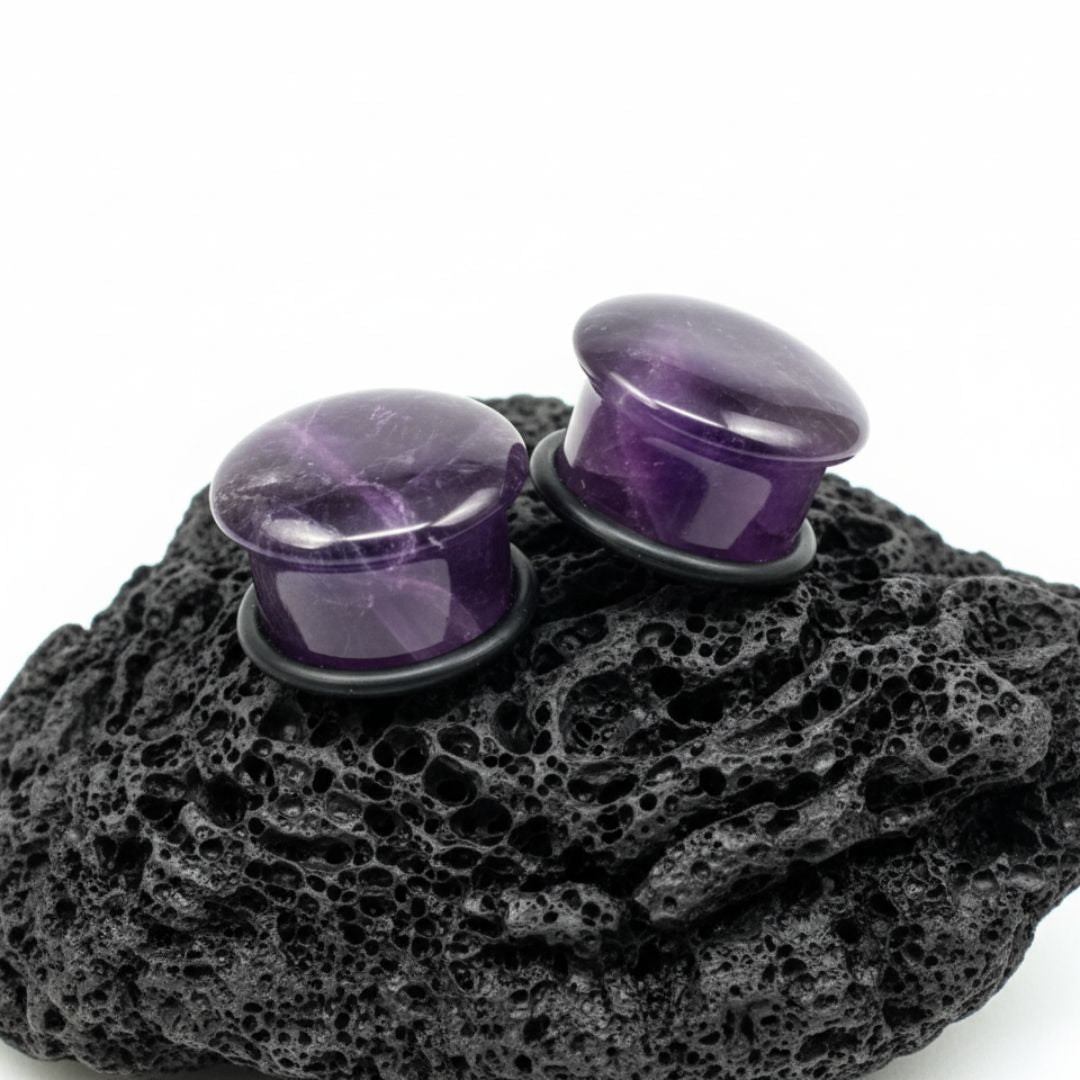 Close-up of deep purple Amethyst stone single flare plugs (gauges) on a white background. Natural alt jewelry for stretched piercings.