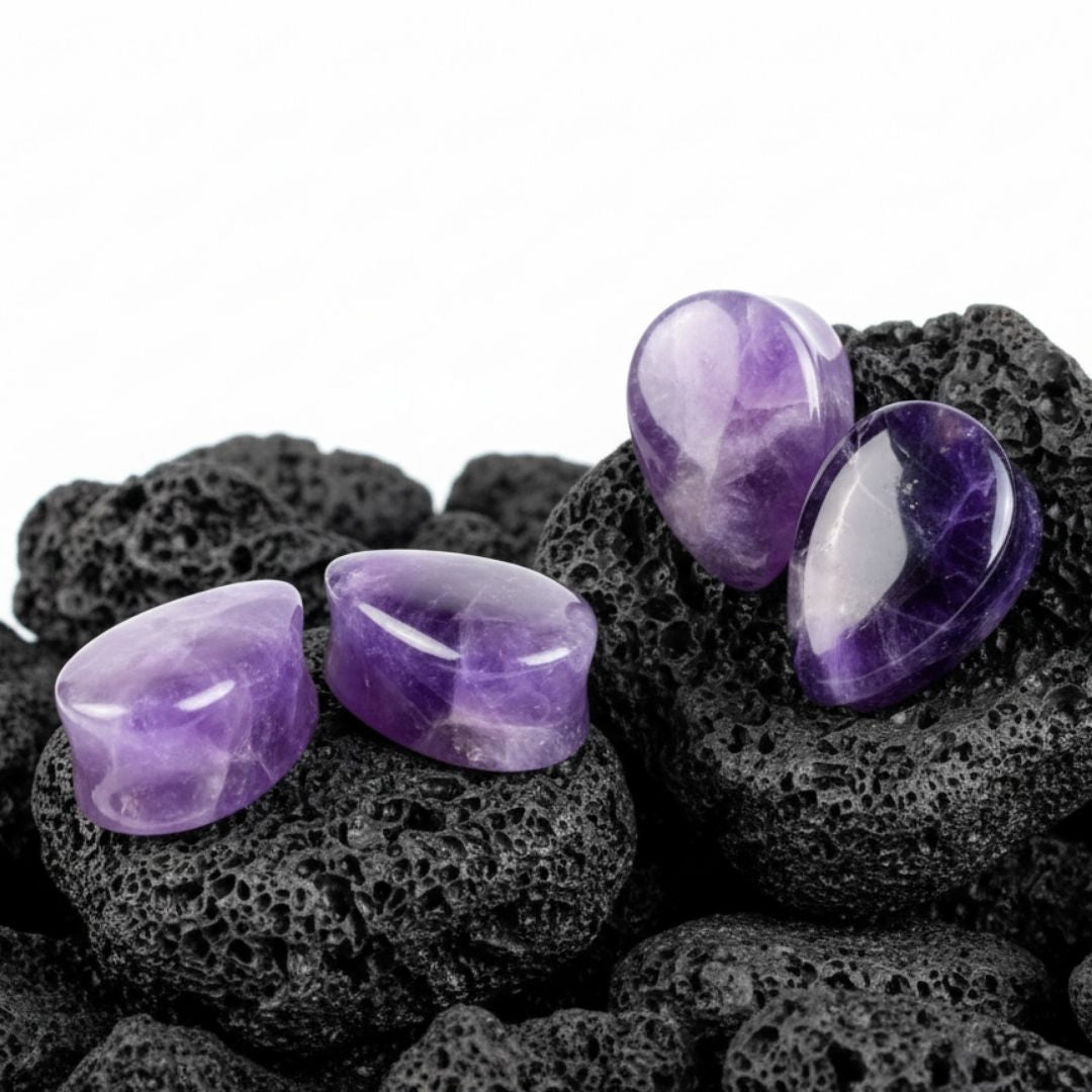 A close-up pair of deep purple, natural Amethyst stone teardrop plugs sitting on a dark surface. Stretched ear gauges jewelry.