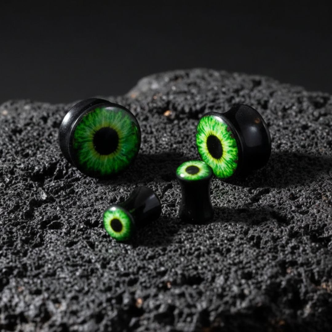 A pair of Basilisk Eye Acrylic Plugs (3mm-30mm) on dark volcanic rock with dramatic light.