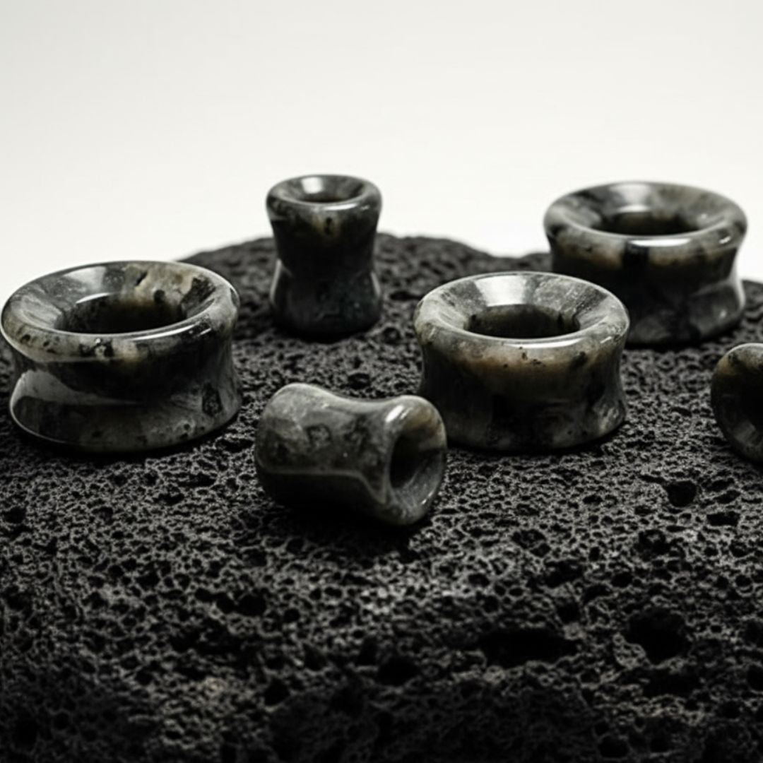 Multiple pairs of Black Labradorite Stone Tunnels (Larvikite) on stone in a white studio.