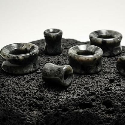 Multiple pairs of Black Labradorite Stone Tunnels (Larvikite) on stone in a white studio.