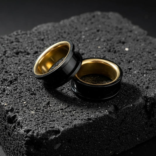 Black and gold PVD plated surgical steel double flared tunnels, shown close up on a stretched ear lobe.