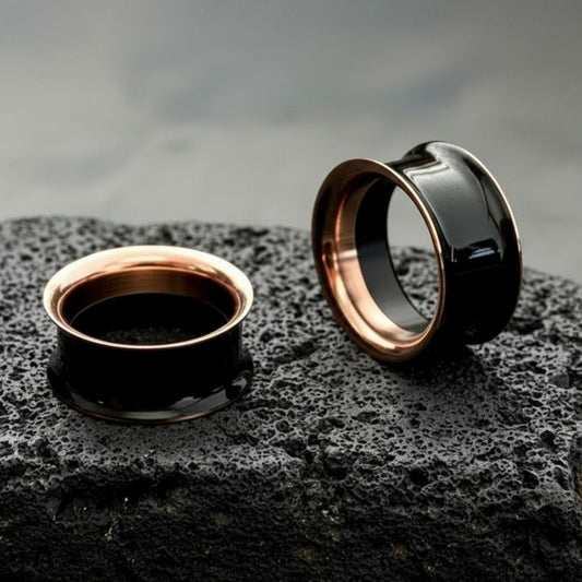 A pair of Black and Rose Gold Tunnels on dark volcanic rock with dramatic side light.