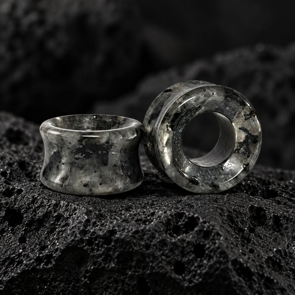 Two dark gray and black marbled stone ear plugs displayed on a textured black rock surface.