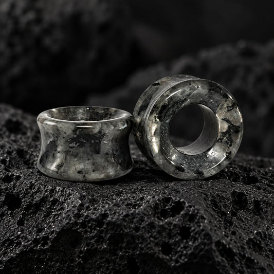 Two dark gray and black marbled stone ear plugs displayed on a textured black rock surface.