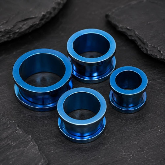 Four metallic blue ear plugs of varying sizes arranged on a dark slate surface.