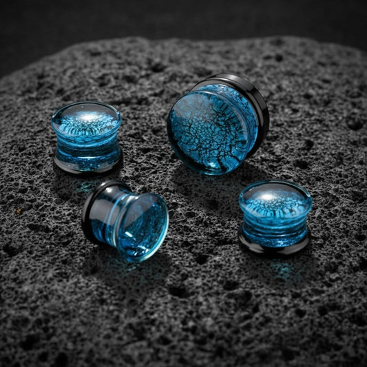 Shattered Glacier Glass Plugs (6mm-25mm) on dark volcanic rock with dramatic lighting.