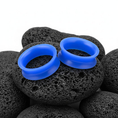 Close-up of deep blue silicone tunnels (gauges) on a white background, highlighting the flexible, lightweight material. Available up to 25mm.