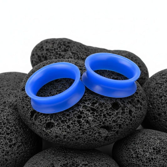 Close-up of deep blue silicone tunnels (gauges) on a white background, highlighting the flexible, lightweight material. Available up to 25mm.