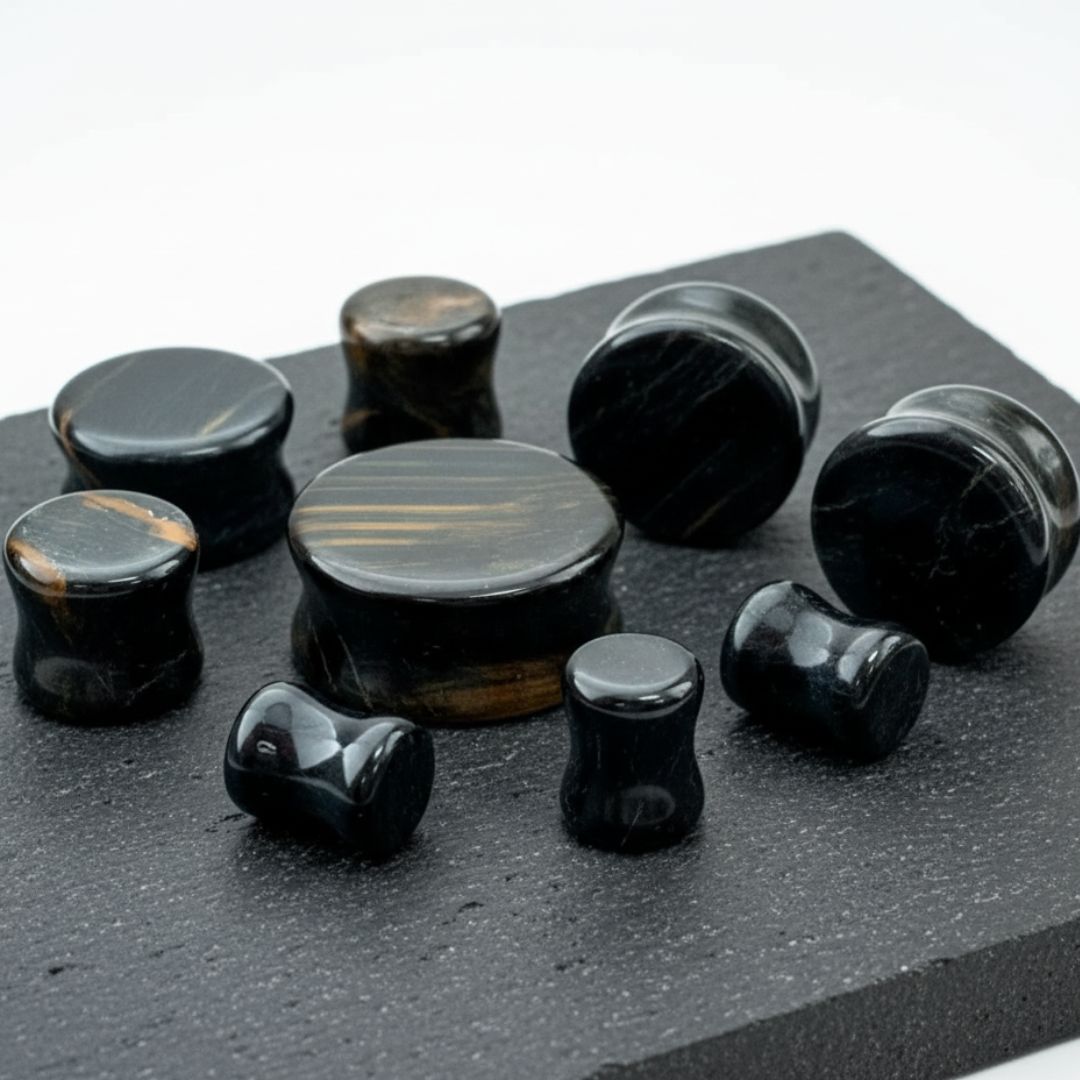 Blue Tigers Eye Stone Plugs, sizes 4mm to 28mm, on a stone against a clean white background.