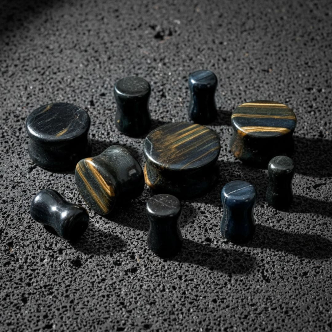Pair of Blue Tigers Eye Stone Plugs, 4mm-28mm, on dark volcanic rock with dramatic light.