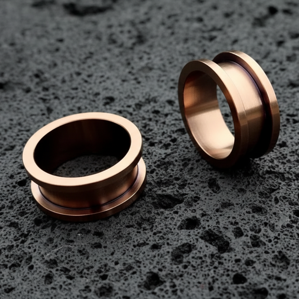 Bronze Screw-Fit Steel tunnels resting on dark volcanic rock with dramatic side light.