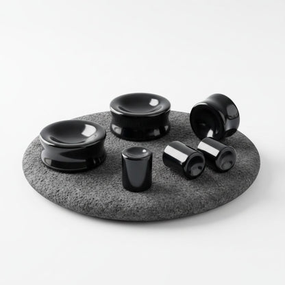 A pair of Concave Onyx Stone Plugs shown on volcanic stone against a white background.