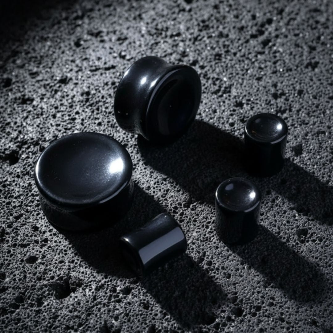 Concave Onyx Stone Plugs (6mm-25mm) resting on dark volcanic rock with dramatic lighting.