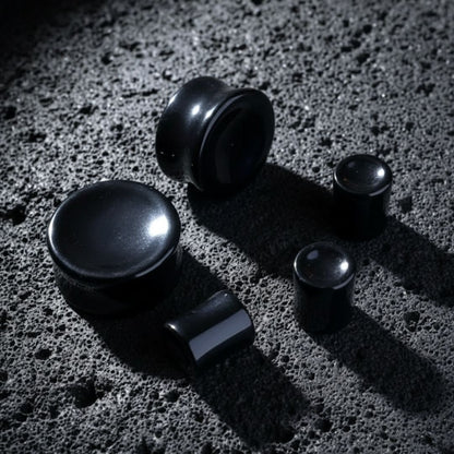 Concave Onyx Stone Plugs (6mm-25mm) resting on dark volcanic rock with dramatic lighting.