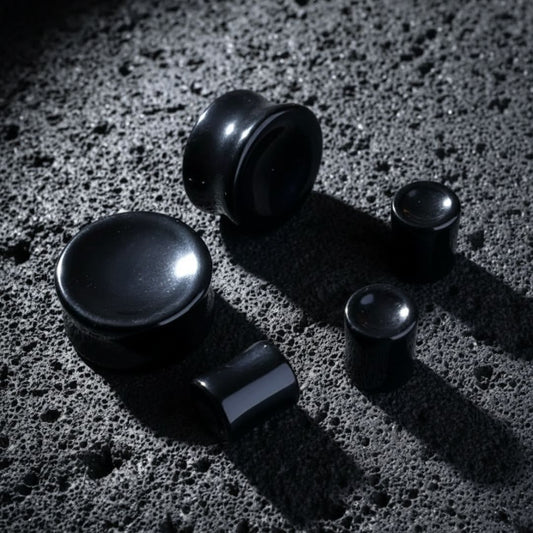 Concave Onyx Stone Plugs (6mm-25mm) resting on dark volcanic rock with dramatic lighting.