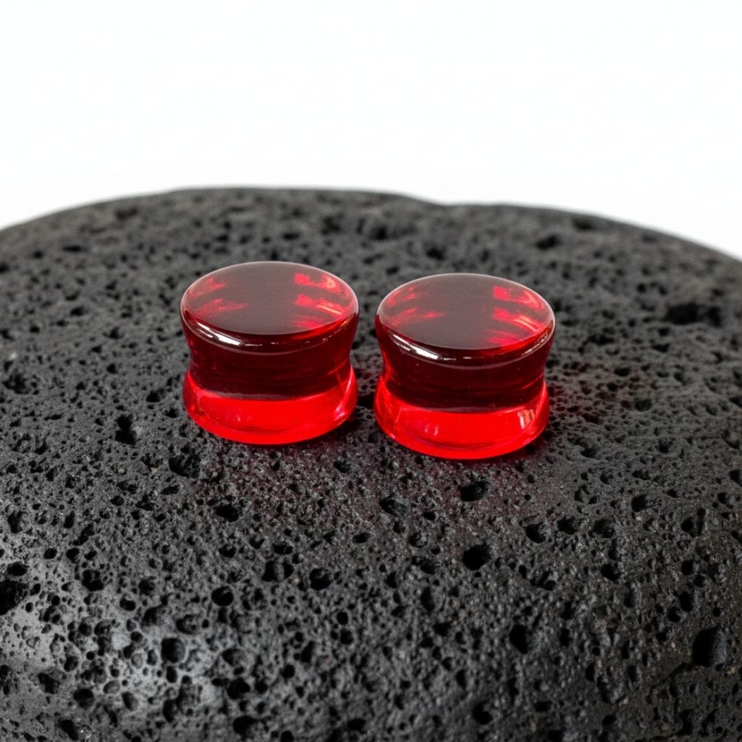 A pair of smooth, polished deep crimson red glass plugs for stretched ear piercings shown against a neutral background.