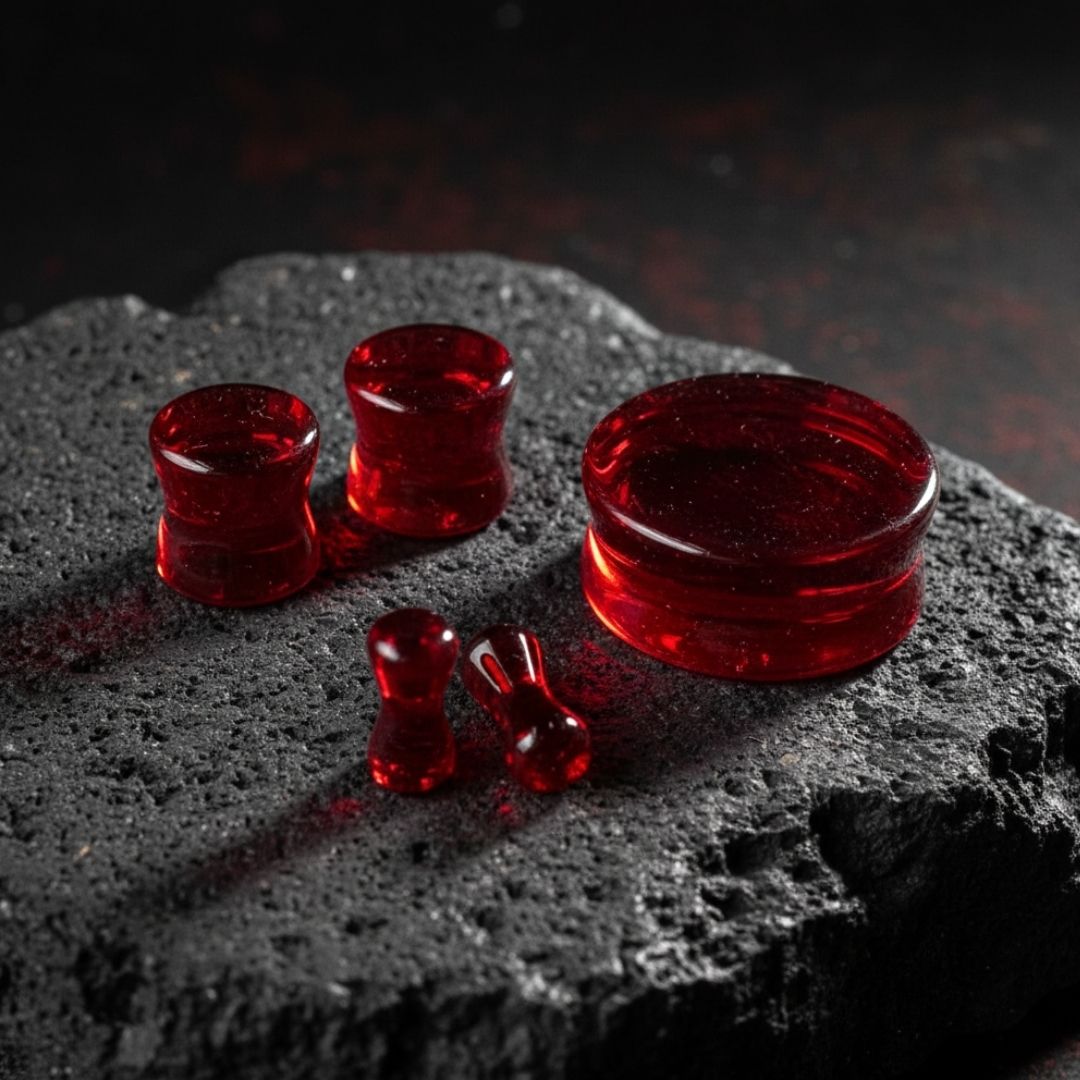 A pair of smooth, polished deep crimson red glass plugs for stretched ear piercings shown against a neutral background.

