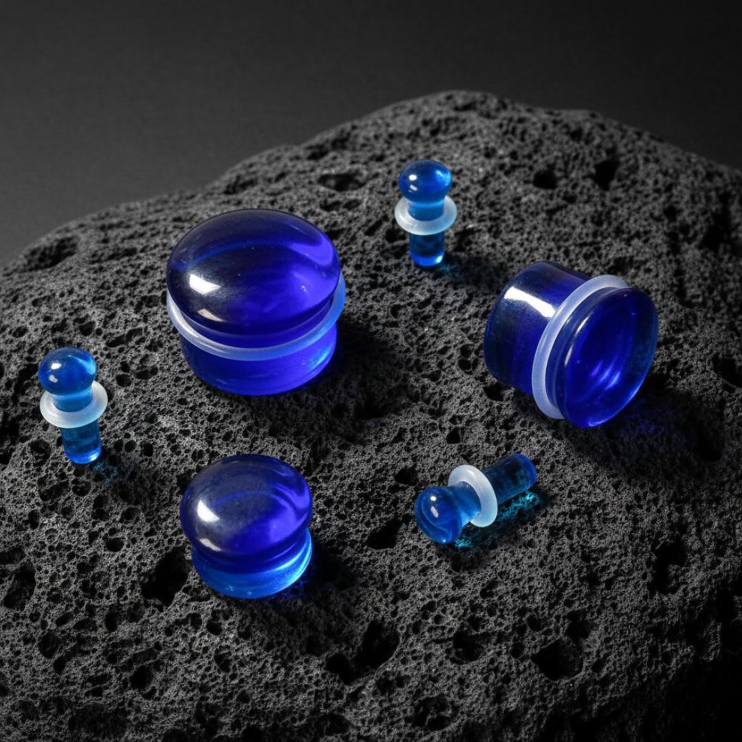Deep Cobalt Glass Plugs (4mm-16mm) sitting on dark volcanic stone with moody side light.