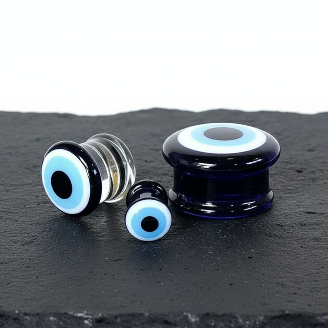 A pair of Warding Eye Glass Plugs resting on volcanic stone on a clean white background.