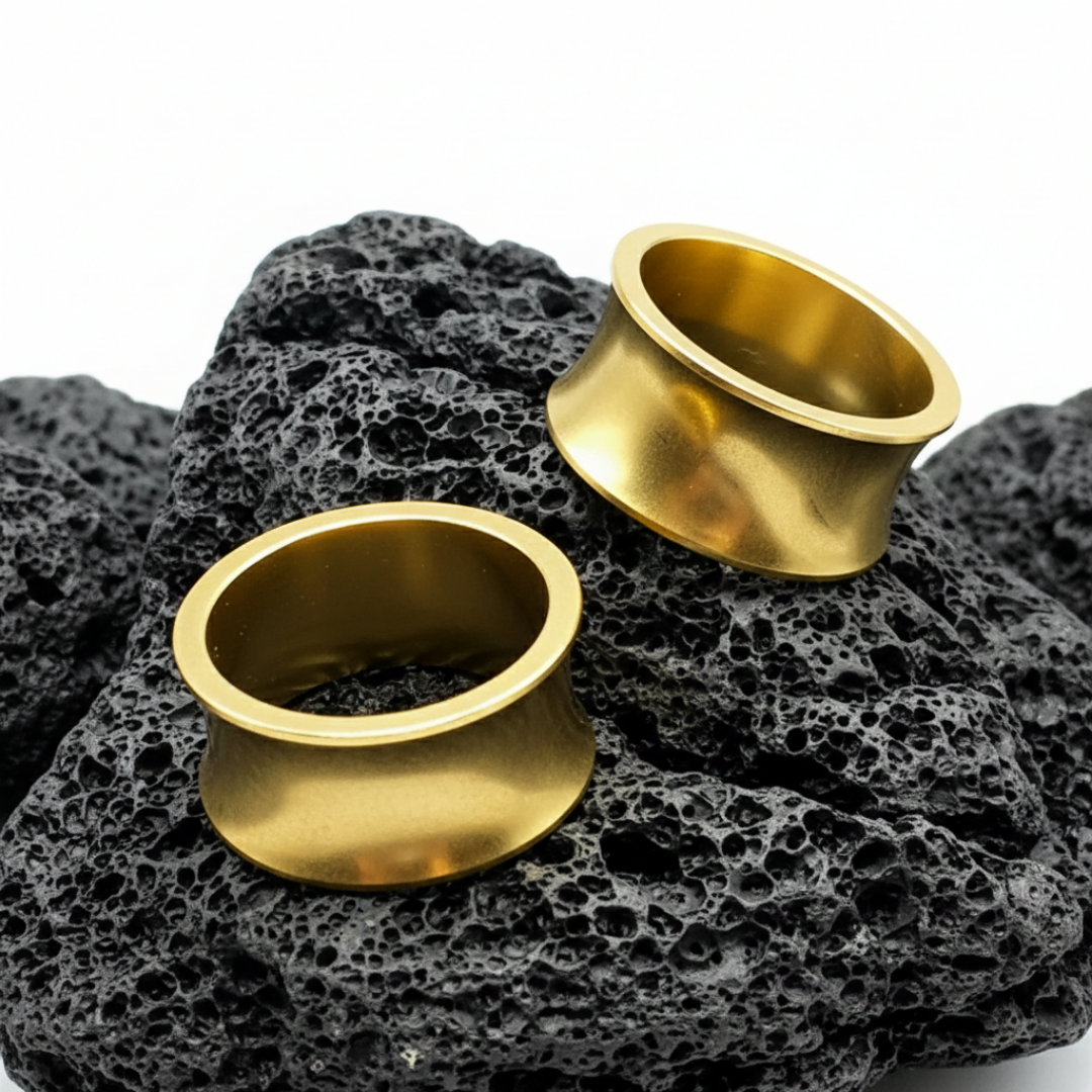 Close-up of Thick Gold PVD Steel Tunnels, double flared gauges displayed against a dark, grungy background.