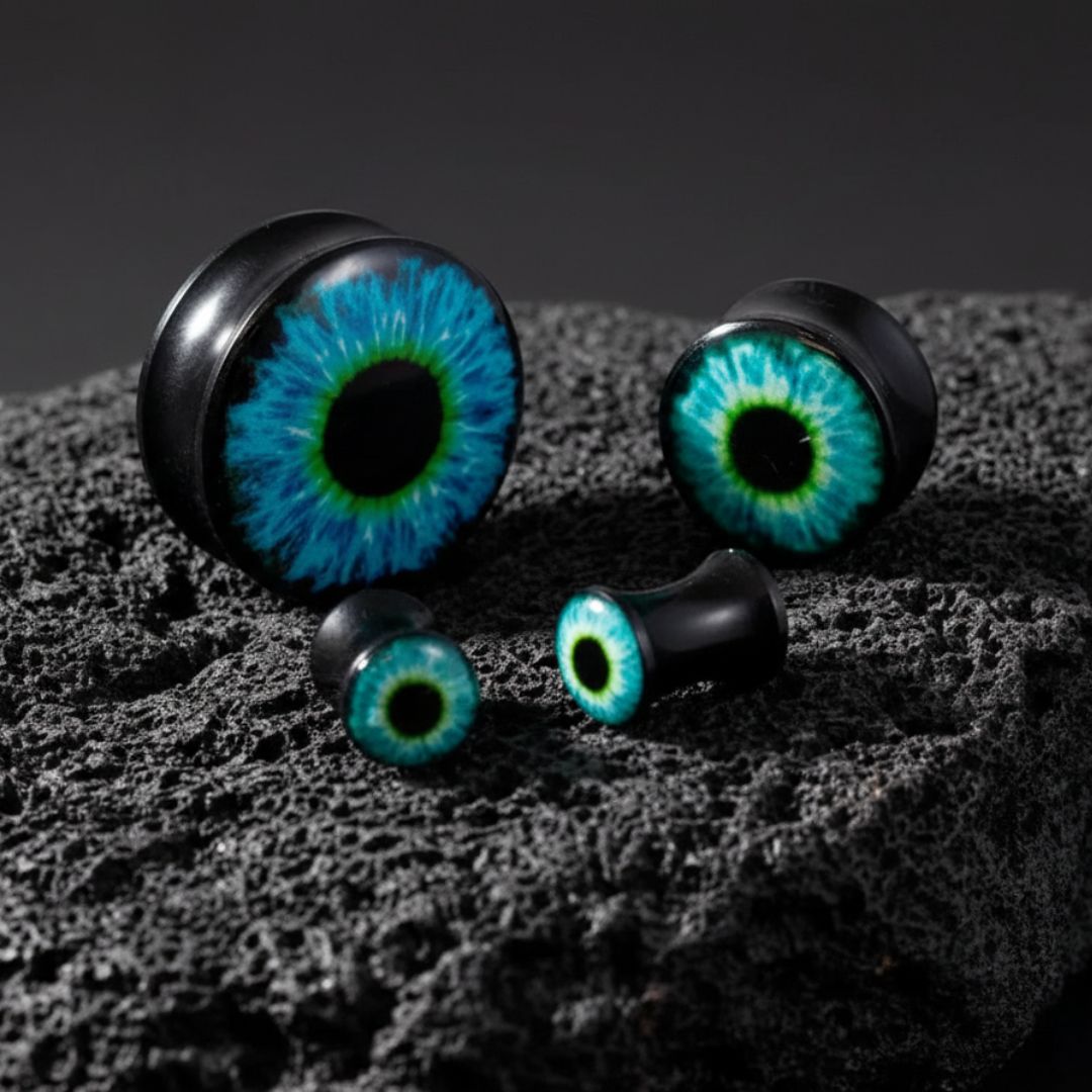 Frost Wyrm Eye Acrylic Plugs (3mm-30mm) on dark volcanic rock with dramatic side light.