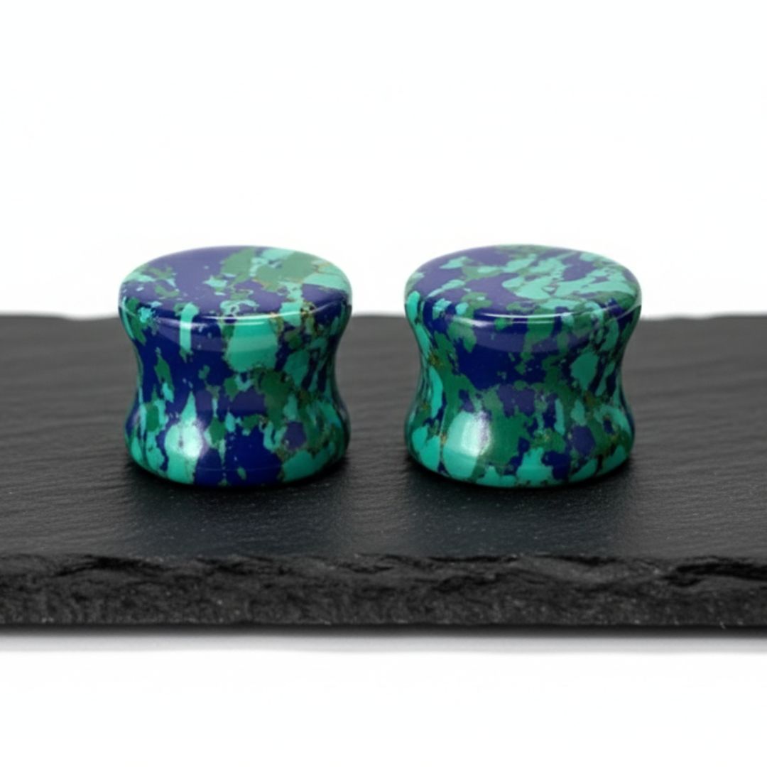 Pair of green and blue patterned ear plugs on a black slate surface.