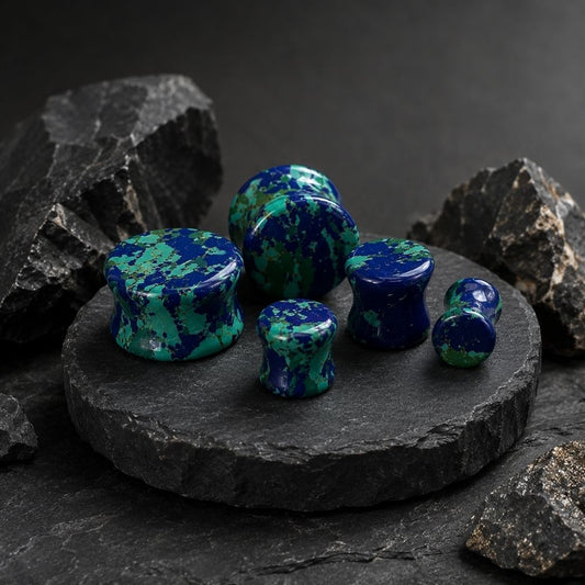 A set of polished blue and green marbled stone plugs arranged on a round black stone slab, with dark rocks around them against a dark studio background.