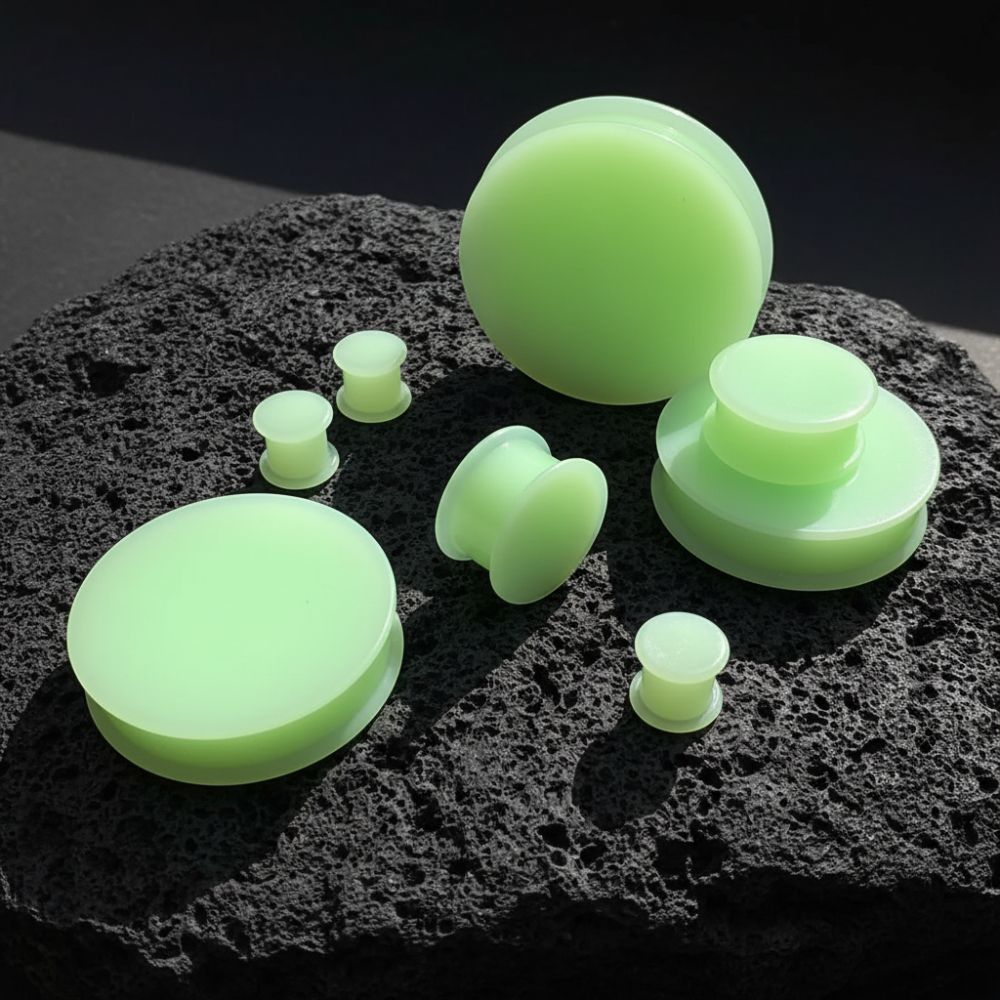Glow in the Dark Silicone Plugs (6mm-51mm) sitting on dark volcanic rock with side light.