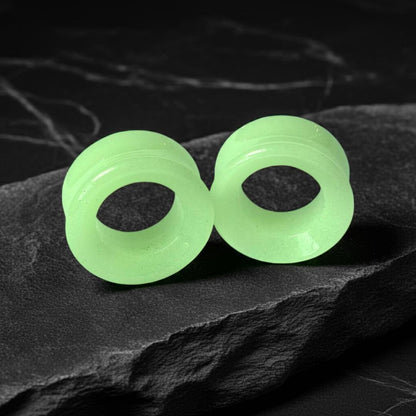 Glow in the dark moonstone tunnels for stretched ears on a gritty black stone background