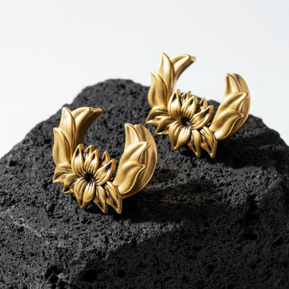 Pair of gold lotus saddle spreaders for stretched ears on a dark textured surface