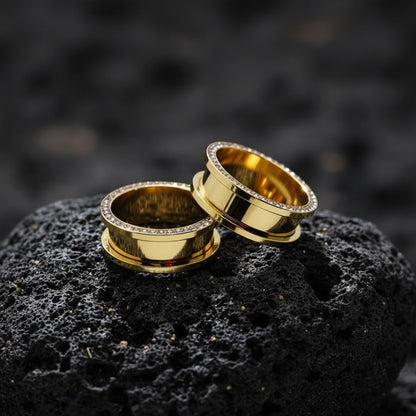 Pair of Gold PVD plated surgical steel tunnels lined with clear gems, shown resting on a dark surface. Available in sizes 2G up to 1 inch.
