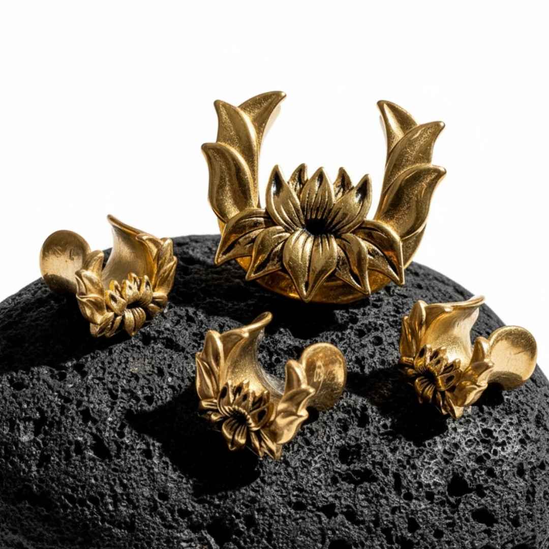 Pair of gold lotus saddle spreaders for stretched ears on a dark textured surface